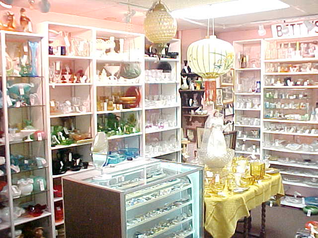 A booth packed with glassware and collectibles on tall white shelves under pendant lamps