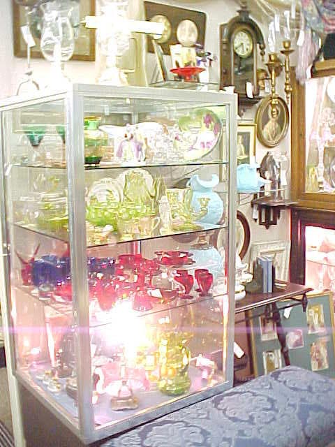 A lit display case of colorful art glass, antique clocks, and framed artwork